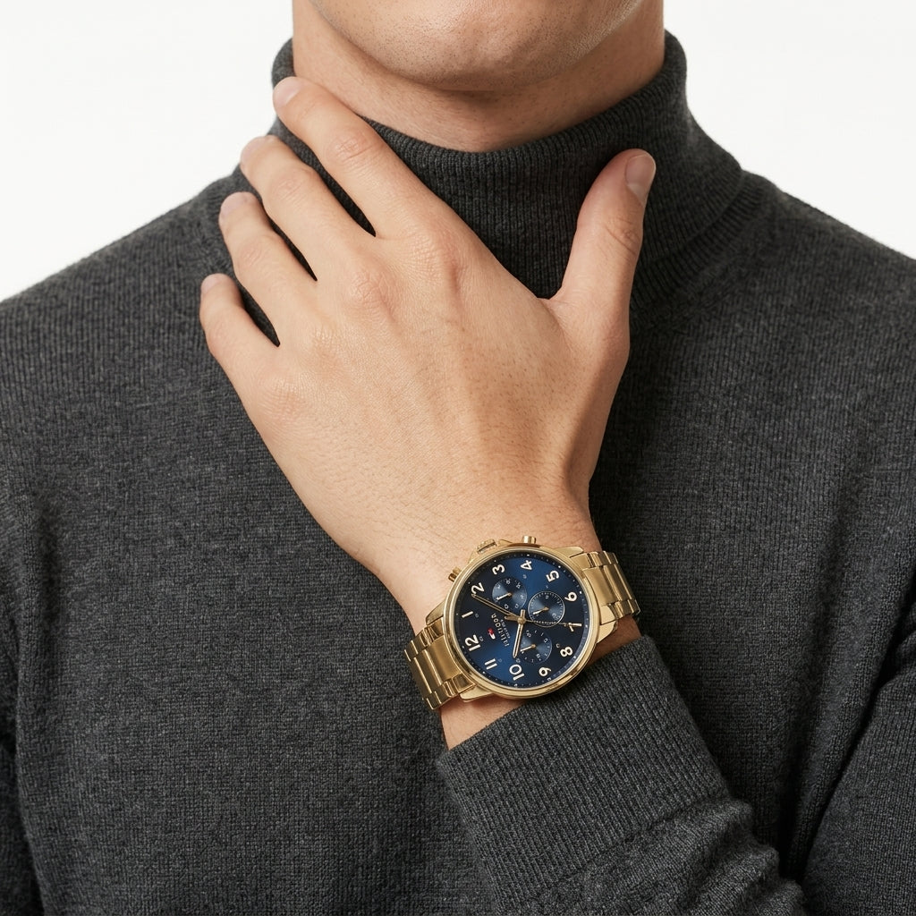 A gold-tone men's watch with a blue dial and blue subdials, worn on a wrist over a dark gray ribbed turtleneck sweater.