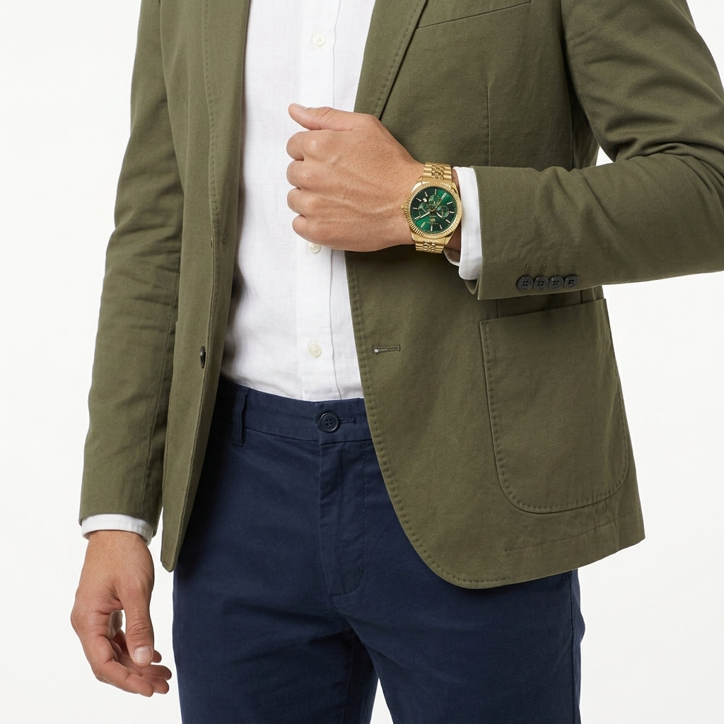 A man wearing an olive green blazer over a white dress shirt and navy trousers, accessorized with a gold-tone watch featuring a green dial.